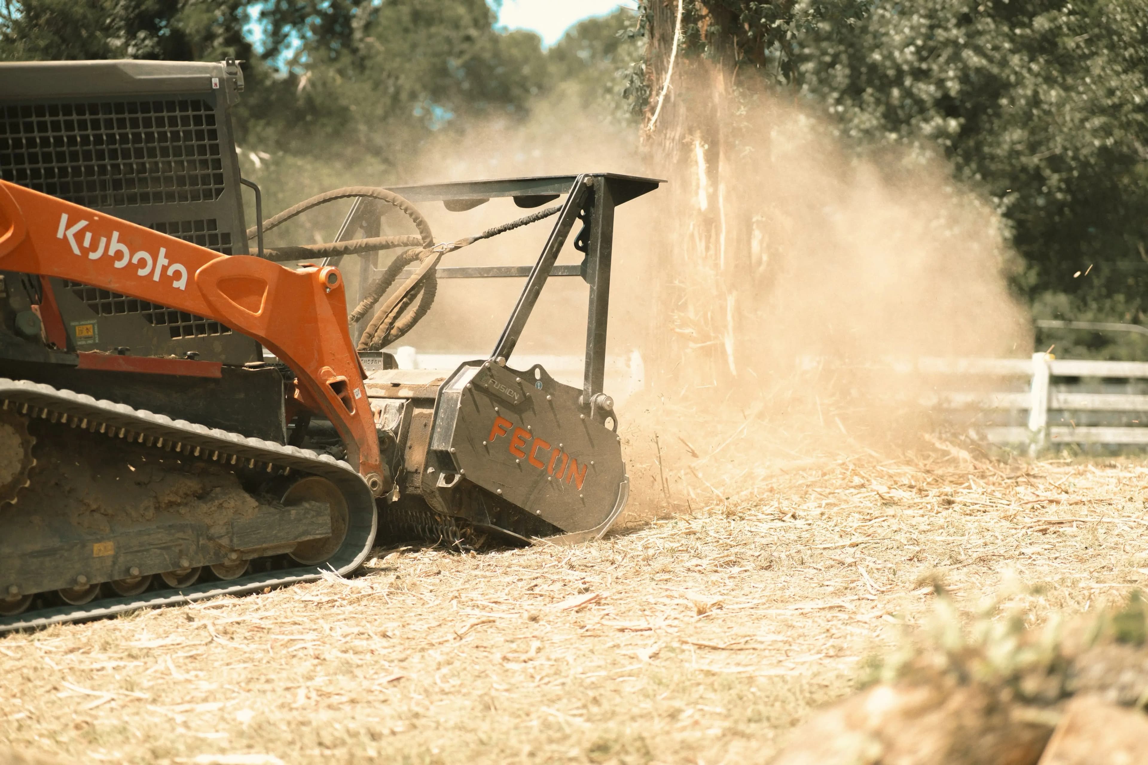 Kubota track loader with a Fecon mulcher clearing land in a cloud of dust