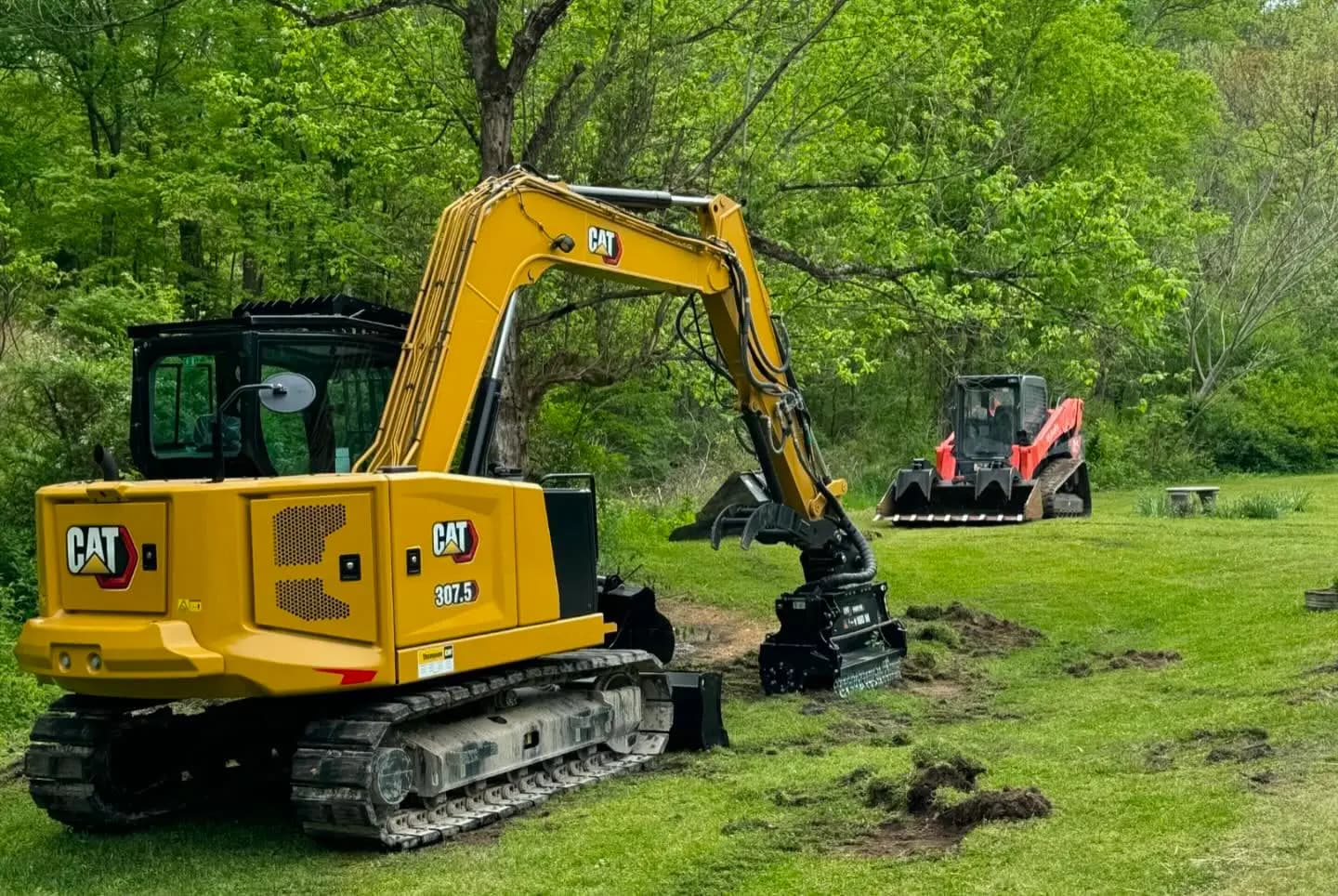 Excavator with a forestry mulching head and a Kubota track loader working a green field