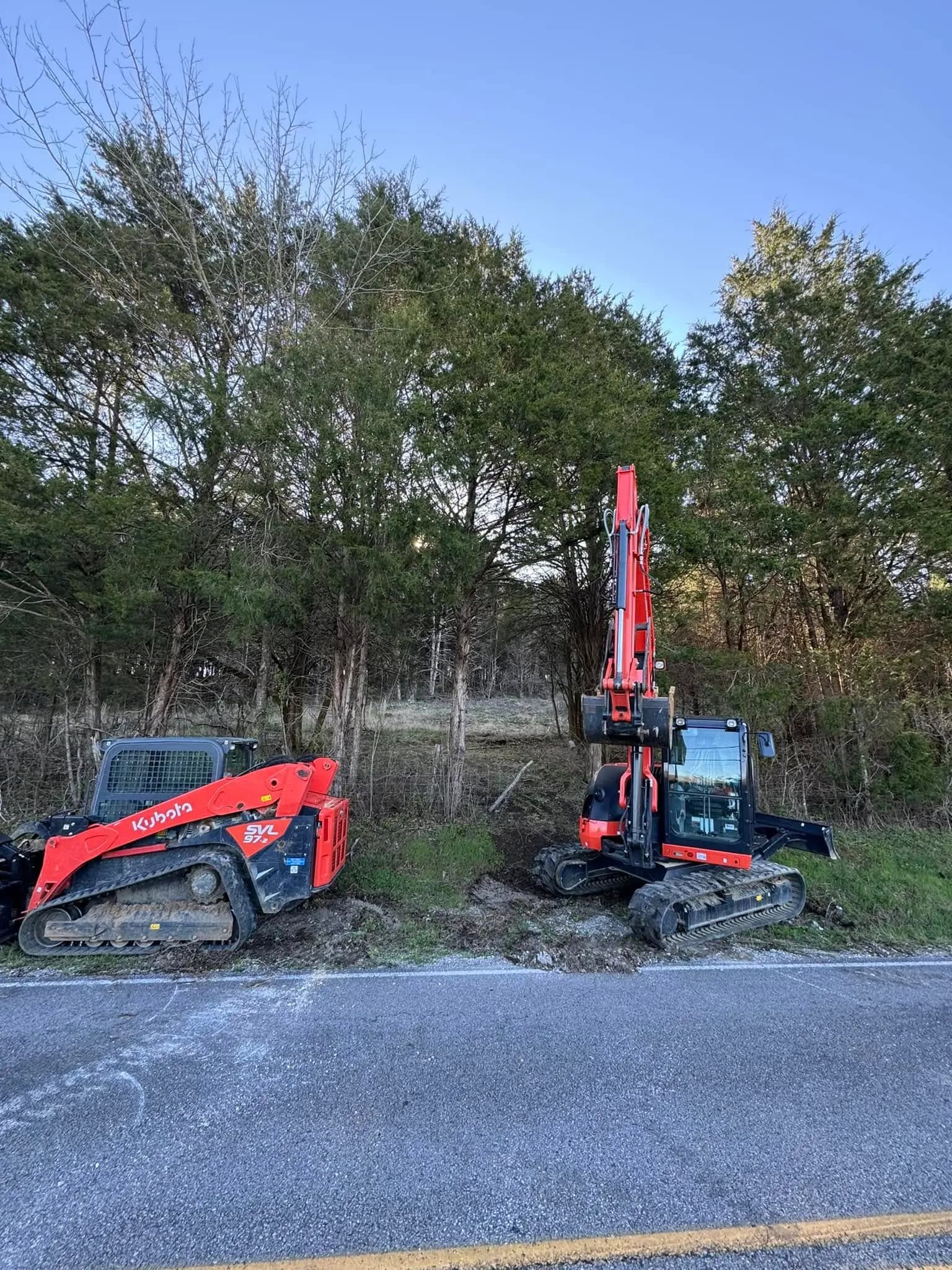 Kubota track loader and excavator opening a cedar-lined roadside entrance