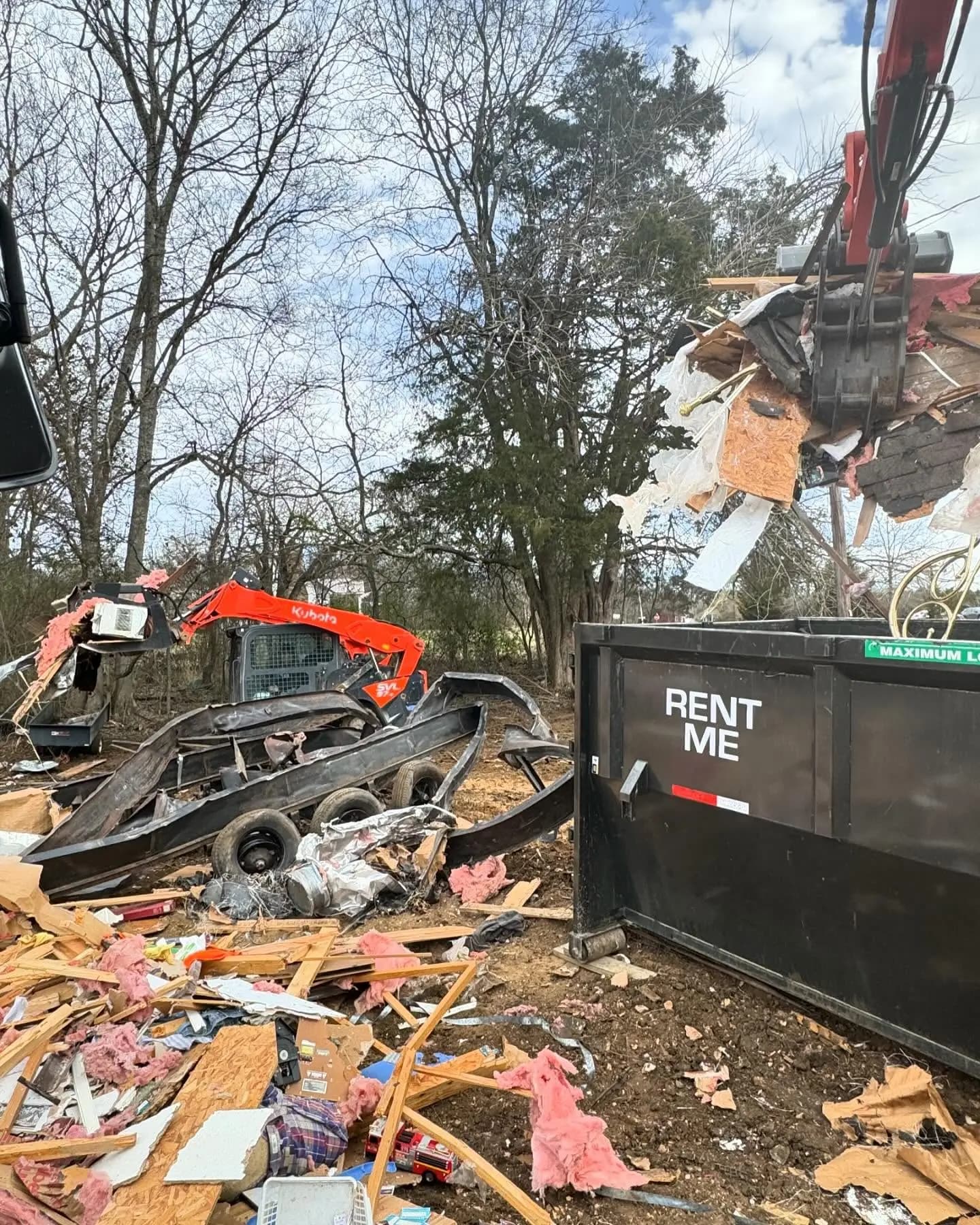 Demolition debris being loaded into a dumpster by a Kubota loader and grapple
