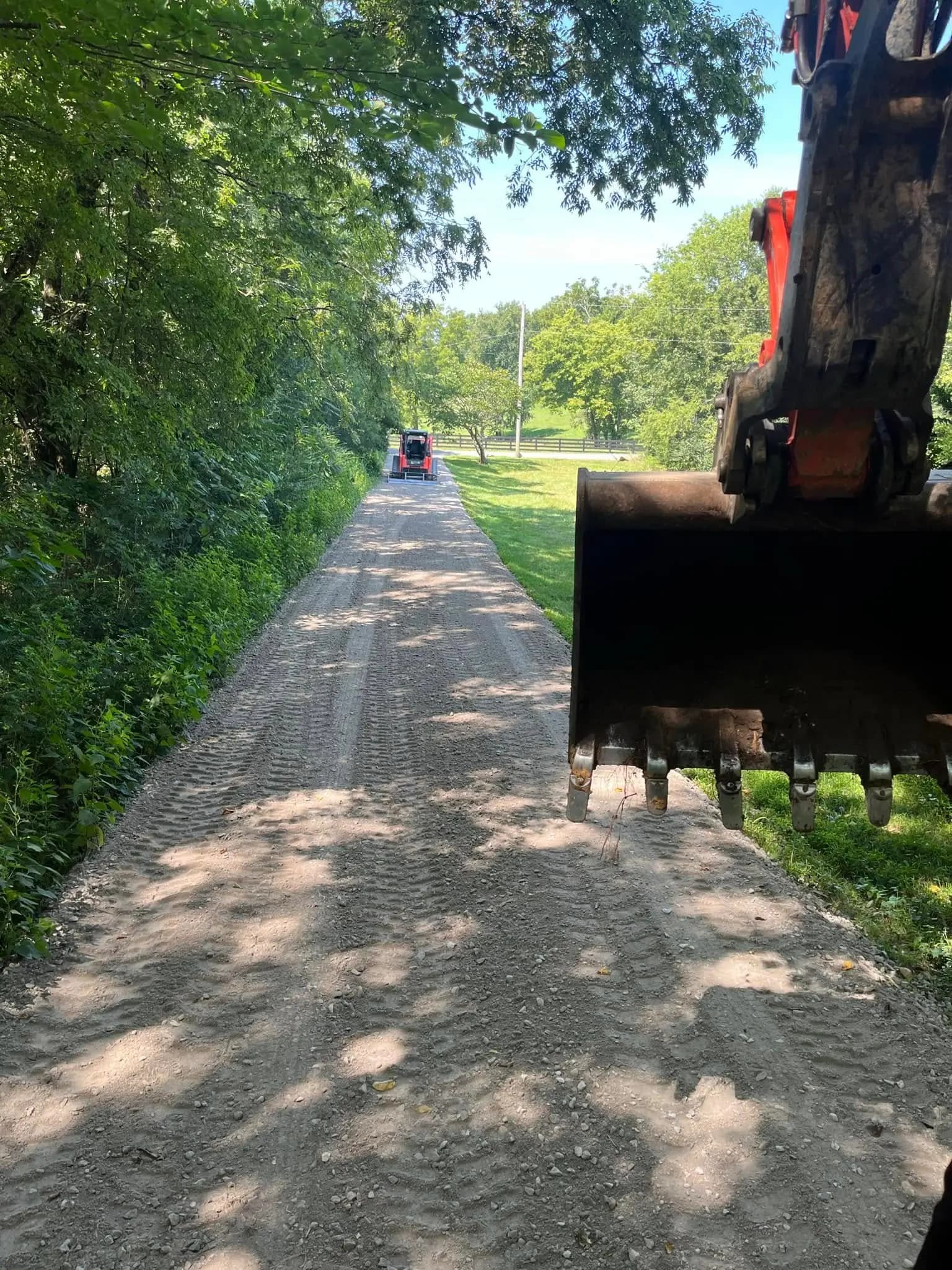 Freshly spread gravel driveway with a track loader grading in the distance