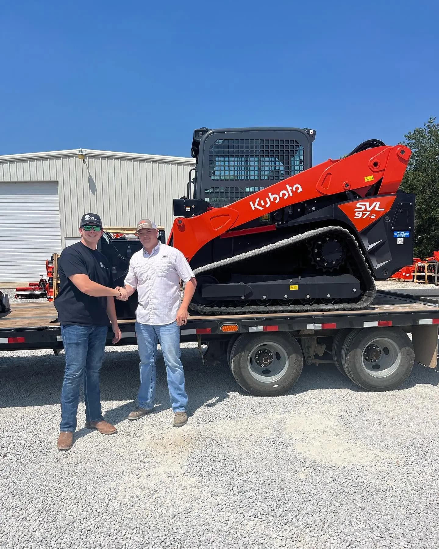 Owner shaking hands in front of a new Kubota SVL97-2 track loader on a trailer